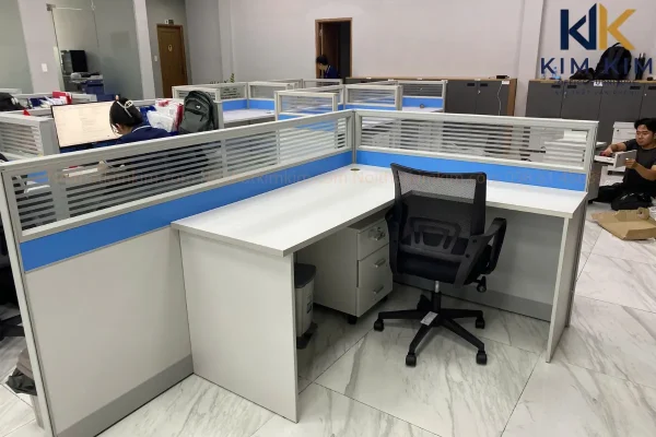 Bàn làm việc chữ L có vách ngăn màu xanh, ghế lưới và hộc tủ tại văn phòng Công ty Button Việt Nam.